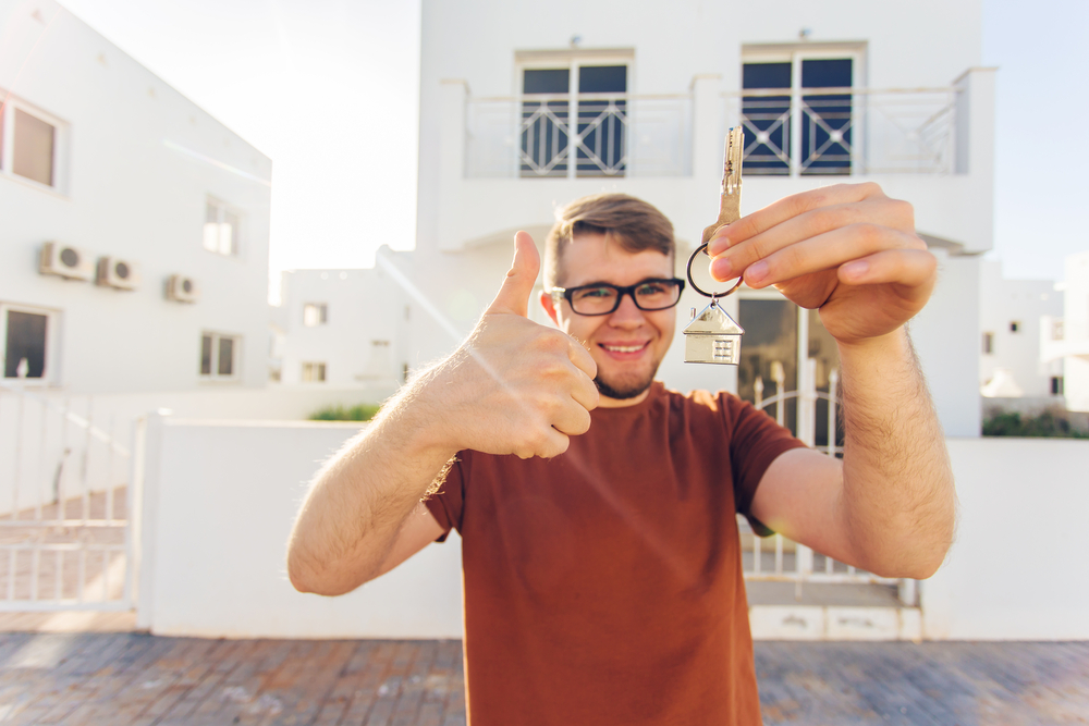 A young man holding house keys in front of his home.